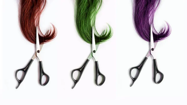 Scissors cutting strands of dyed red, green and purple hair — Stock Photo, Image