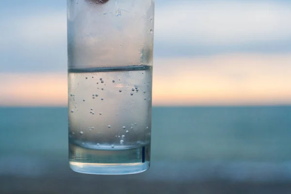 Glass of sparkled water. On the background is a blue sea and ora