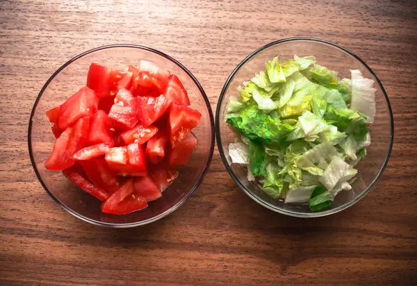 Gesneden tomaten en sla voor het bereiden van voedsel in glazen kommen op wo — Stockfoto