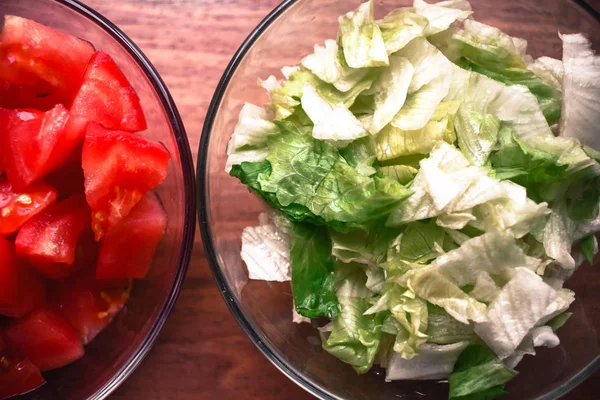 Gesneden tomaten en sla voor het bereiden van voedsel in glazen kommen op wo — Stockfoto