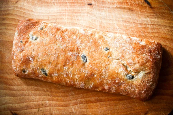 Хлебная булочка с оливками на деревянной доске на деревянном фоне — стоковое фото