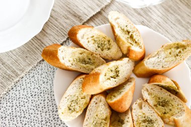 Beyaz bir plaka üzerinde yeşil pesto ile sarımsak ekmek dilimleri. Parlak pi