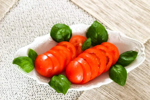 Frisch geschnittene rote reife Tomaten mit Basilikum auf einem weißen Teller zubereitet — Stockfoto