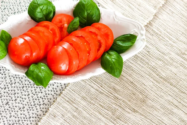 Frisch geschnittene rote reife Tomaten mit Basilikum auf einem weißen Teller zubereitet — Stockfoto