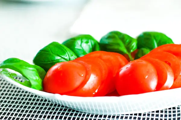 Frisch geschnittene rote reife Tomaten mit Basilikum auf einem weißen Teller zubereitet — Stockfoto
