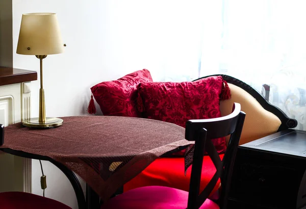 Номер со столом с коричневой скатертью, лампой и красными подушками — стоковое фото
