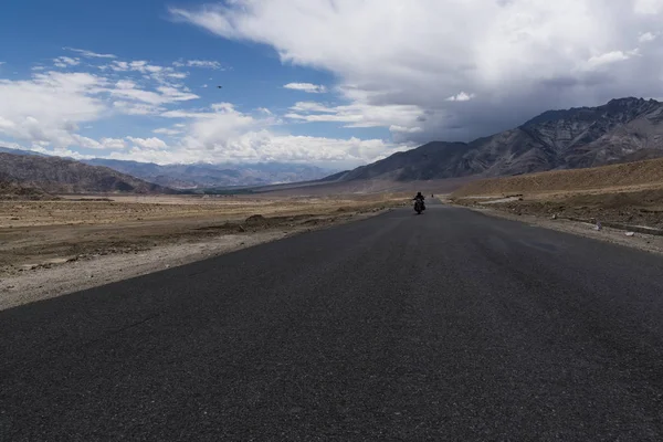 Motocicleta se movendo em uma estrada reta em planícies do deserto de Ladakh . — Fotografia de Stock