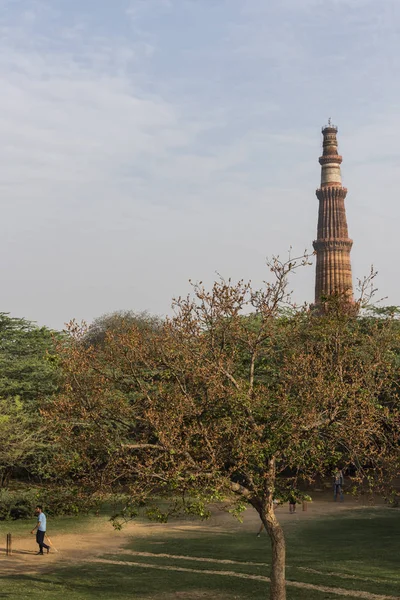 Gente jugando al cricket en el parque arqueológico Mehrauli y Qutub Minar visto de fondo . — Foto de Stock
