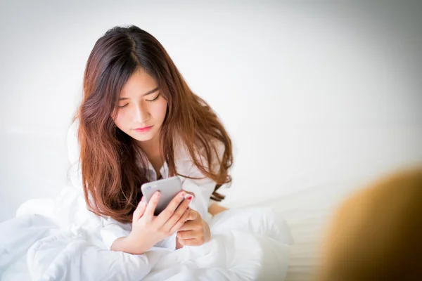 Mädchen mit Handy zu Hause auf dem Bett liegend Stockbild