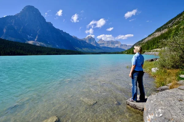 Mujer mirando la hermosa vista del lago turquesa claro y las montañas rocosas . — Foto de Stock