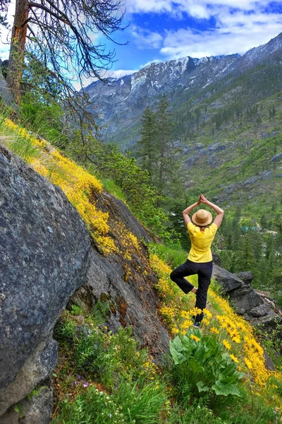 Frau in Yoga-Pose in den Bergen inmitten gelber Wildblumen im Frühling. — Stockfoto