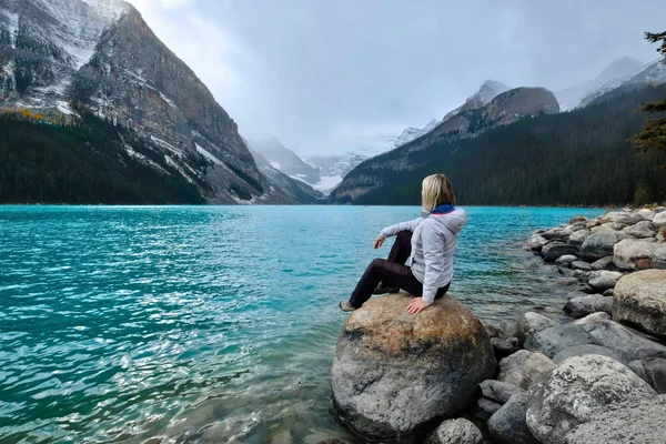 Γυναίκα κάθεται στο βράχο στη λίμνη Louise και απολαμβάνοντας τη θέα του παγετώνα Victoria. — Φωτογραφία Αρχείου