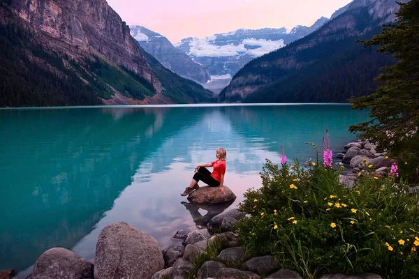 Vrouw zitten op rots in Lake Louise bij zonsondergang. — Stockfoto