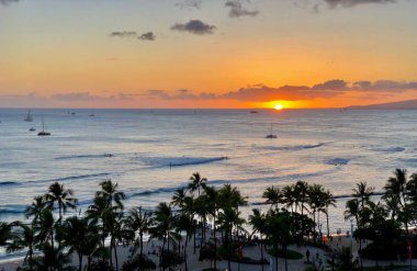 Wikiki Beach, Hololulu 'dan Pasifik Okyanusu üzerinde gün batımı. Gün batımında palmiye ağaçları, katamaranlar ve sörfçüler. Hawaii mi? Amerika Birleşik Devletleri
