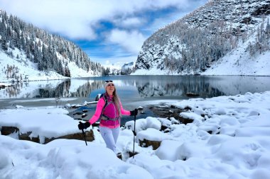 Kar altında kar ayakkabısı giyen mutlu bir kadın. Agnes Gölü 'nün yanında kar yağdıktan sonraki güneşli bir günde dağların ve ağaçların yansımalarıyla. Banff Ulusal Parkı 'ndaki Louise Gölü bölgesinde. Alberta. Kanada.