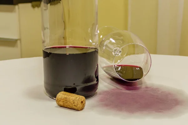 Червоне вино розлилося зі скла над білою скатертиною з пляшкою Стокове Зображення