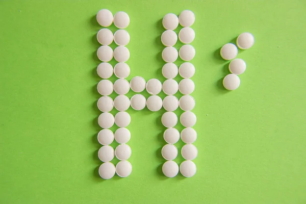 Sign H, for hospital, made by white pills on green background — Stock Photo, Image