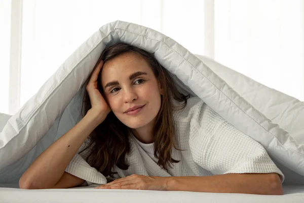 Hermosa mujer bajo una manta blanca en la cama . — Foto de Stock