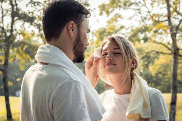 Young man wiped the sweat for his girlfriend after exercising together with tenderness. Concept couples exercise in the park. Young couples are wiping sweat after exercising in the park.