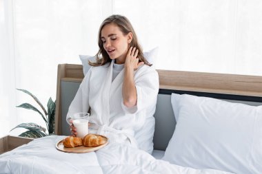 Kahvaltı etmeye hazır beyaz pijamalı güzel bir kadın sabahları yataktaki yatak odasında uyandıktan sonra süt ve kruvasandır. Kafkasyalı kız sabah uyandıktan sonra süt içiyor..