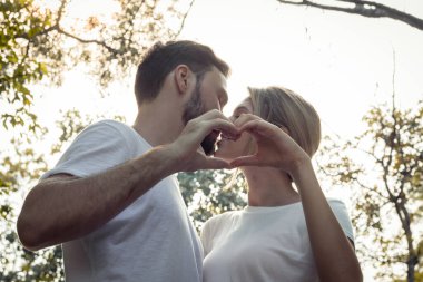 Öpüşen genç aşıklar parkta bir kalp oluşturmak için el ele tutuşmaya hazır. Genç çiftler parkta birbirlerine sevgilerini gösterirler. Parktaki genç çift kavramı.