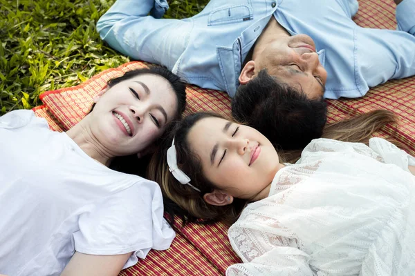 Parents and children at the squat and smiling on the mat in the park. Asian family lying on a mat in the park.