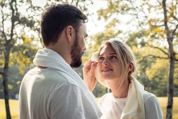 Young man wiped the sweat for his girlfriend after exercising together with tenderness. Concept couples exercise in the park. Young couples are wiping sweat after exercising in the park.