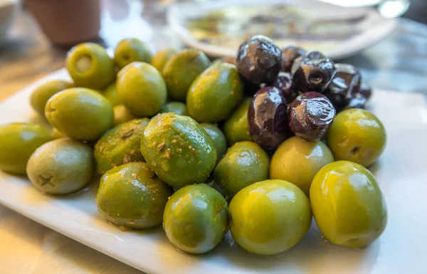 Bar masasında küçük bir tabakta zeytin. Tipik İspanyol yeşili ve siyah zeytin. — Stok fotoğraf