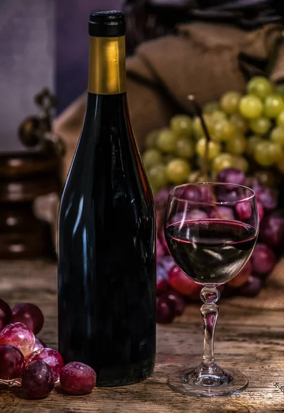 Copa de vino tinto de uvas maduras y botella de vino sobre fondo de madera — Foto de Stock