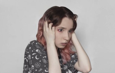 Elleri kafasında, pembe saçlı, genç, panik bir kadın.