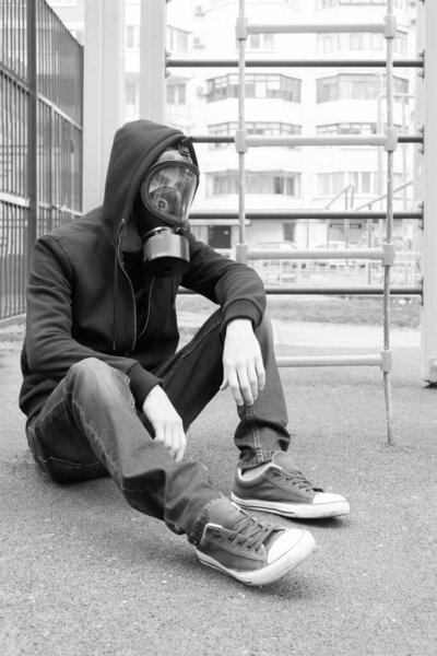 A lonely man in a respiratory mask sits on a ground on a deserted city during a coronavirus epidemic. Black and white photography. Selective and soft focus.