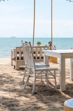 Beyaz sandalye ve cl ve mavi okyanus manzaralı bir sahilde tablo
