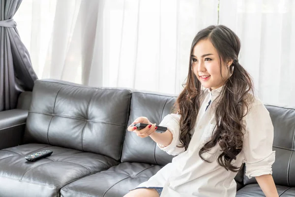 Jovem mulher asiática mudando canal de tv em casa na sala de estar — Fotografia de Stock