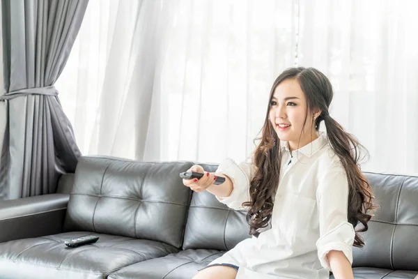 Jovem mulher asiática mudando canal de tv em casa na sala de estar — Fotografia de Stock