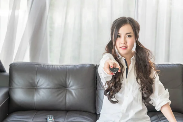 Mladá asijská žena mění televizní kanál doma v obývacím pokoji — Stock fotografie