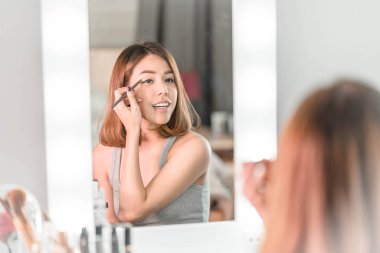 Genç güzel Asyalı ayna yakınındaki makyaj yapma kadın