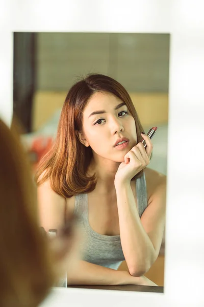 Jovem bela mulher asiática fazendo maquiagem perto do espelho — Fotografia de Stock