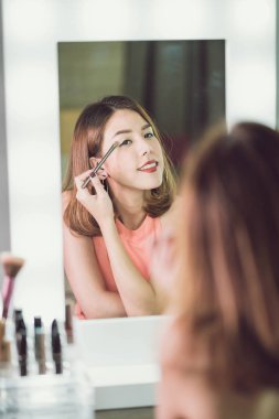 Genç güzel Asyalı ayna yakınındaki makyaj yapma kadın