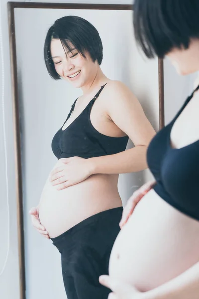 Молодая красивая азиатская беременная женщина прикасается к животу дома — стоковое фото