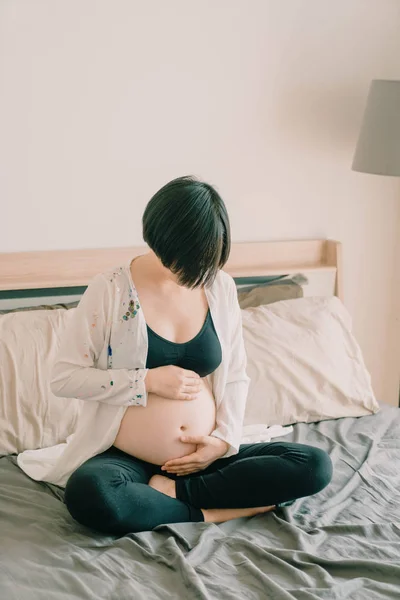 Joven hermosa mujer embarazada asiática acostada en la cama y tocando h — Foto de Stock