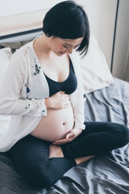 Yatakta yatan ve h dokunmadan genç güzel Asyalı hamile kadın