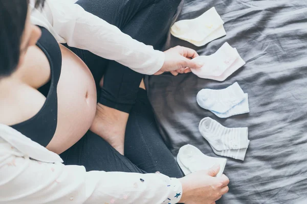 Vientre de la mujer embarazada con las manos la elección de los calcetines de bebé — Foto de Stock