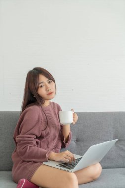 Asian woman using laptop on sofa in living room 
