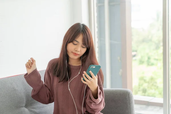 Aziatische vrouw met behulp van smartphone op grijze bank in de woonkamer — Stockfoto