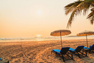 Güneş doğarken palmiye ağacı ve deniz plajı olan şemsiye koltuğu plajı - tatil ve tatil konsepti