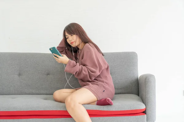 美しいアジアの女性がリビングでグレーのソファにスマートフォンを使って — ストック写真