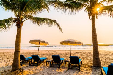 Güneş doğarken palmiye ağacı ve deniz plajı olan şemsiye koltuğu plajı - tatil ve tatil konsepti