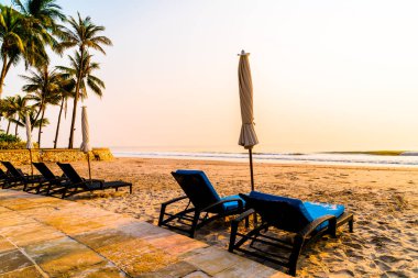 Güneş doğarken palmiye ağacı ve deniz plajı olan şemsiye koltuğu plajı - tatil ve tatil konsepti