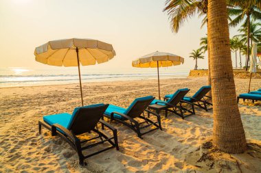 Güneş doğarken palmiye ağacı ve deniz plajı olan şemsiye koltuğu plajı - tatil ve tatil konsepti