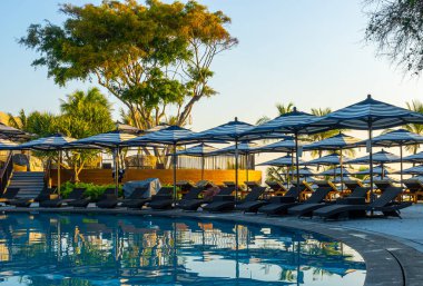 Seyahat tatili konsepti için otel tatil beldesinde yüzme havuzunun etrafında şemsiye ve sandalye.